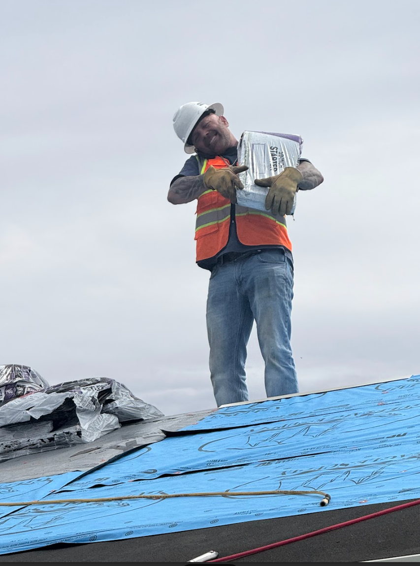 Force 5 Roofing crew member in hard hat and safety vest on a residential roof, holding a fresh bundle of shingles ready to install