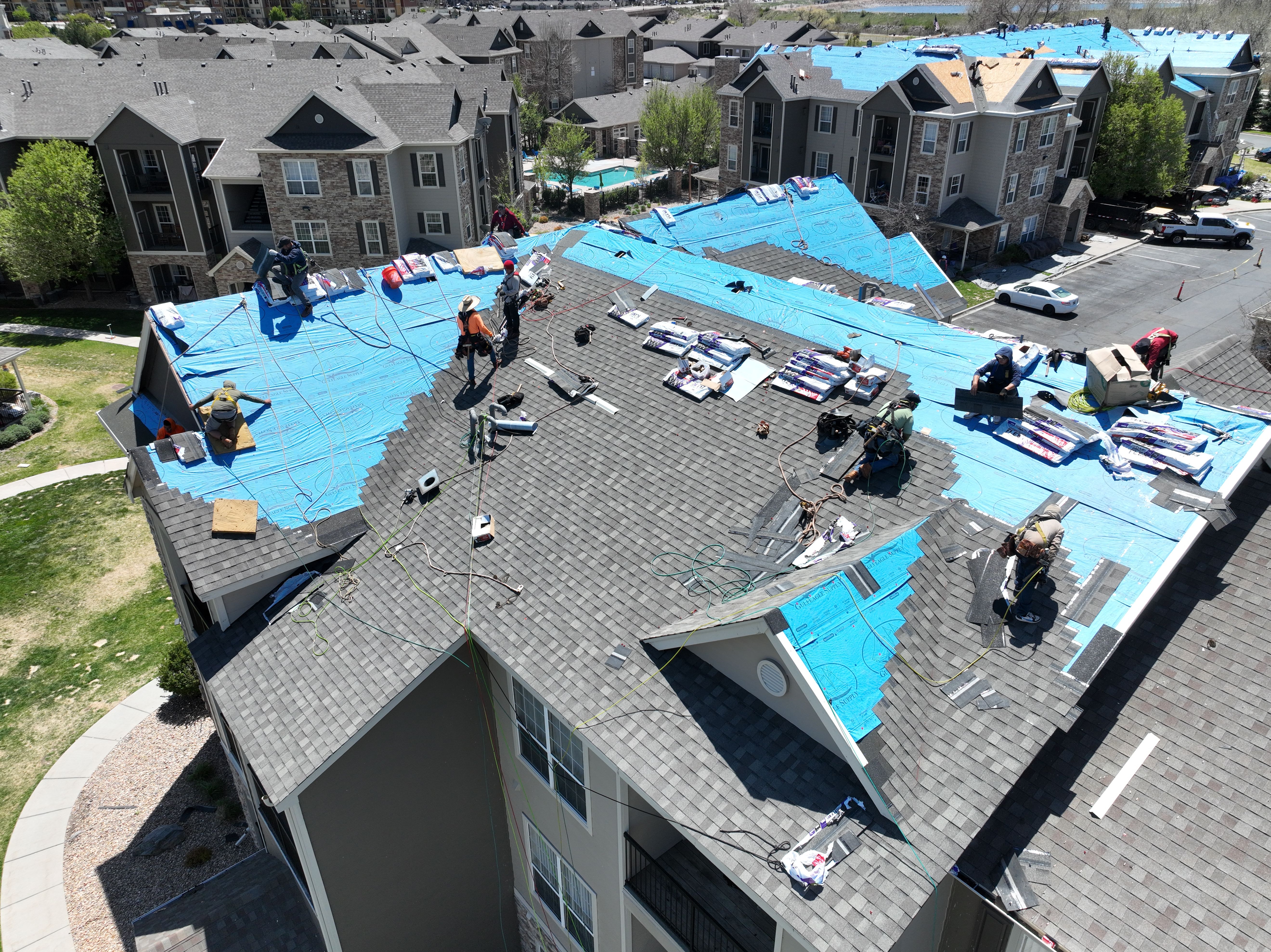 Aerial view of Force 5 Roofing crew working on a full multifamily apartment complex re-roof in Denver Metro — multiple buildings staged with synthetic underlayment and shingle bundles