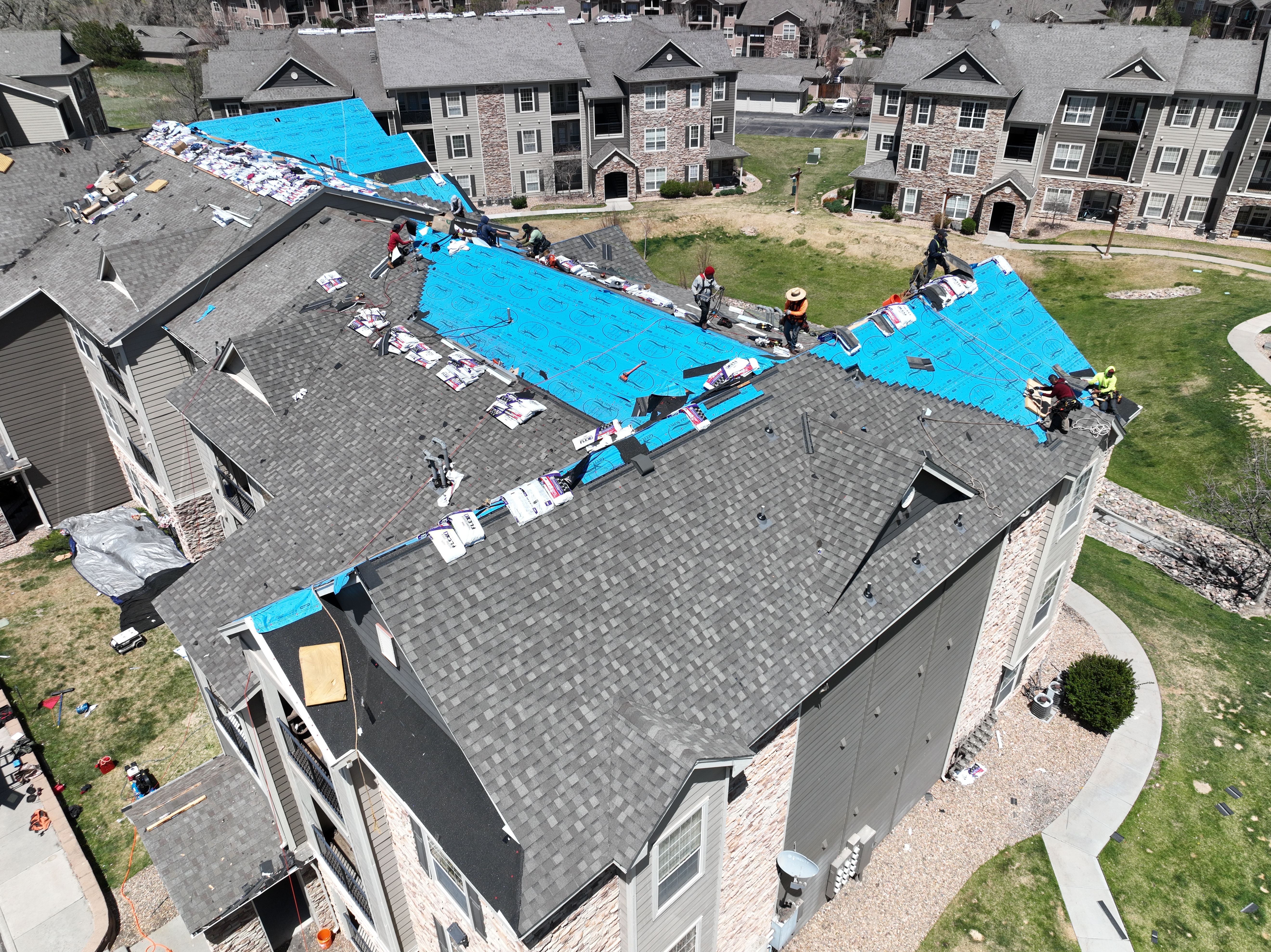 Aerial of Force 5 Roofing crew laying synthetic underlayment and staging shingle bundles across a multifamily apartment building