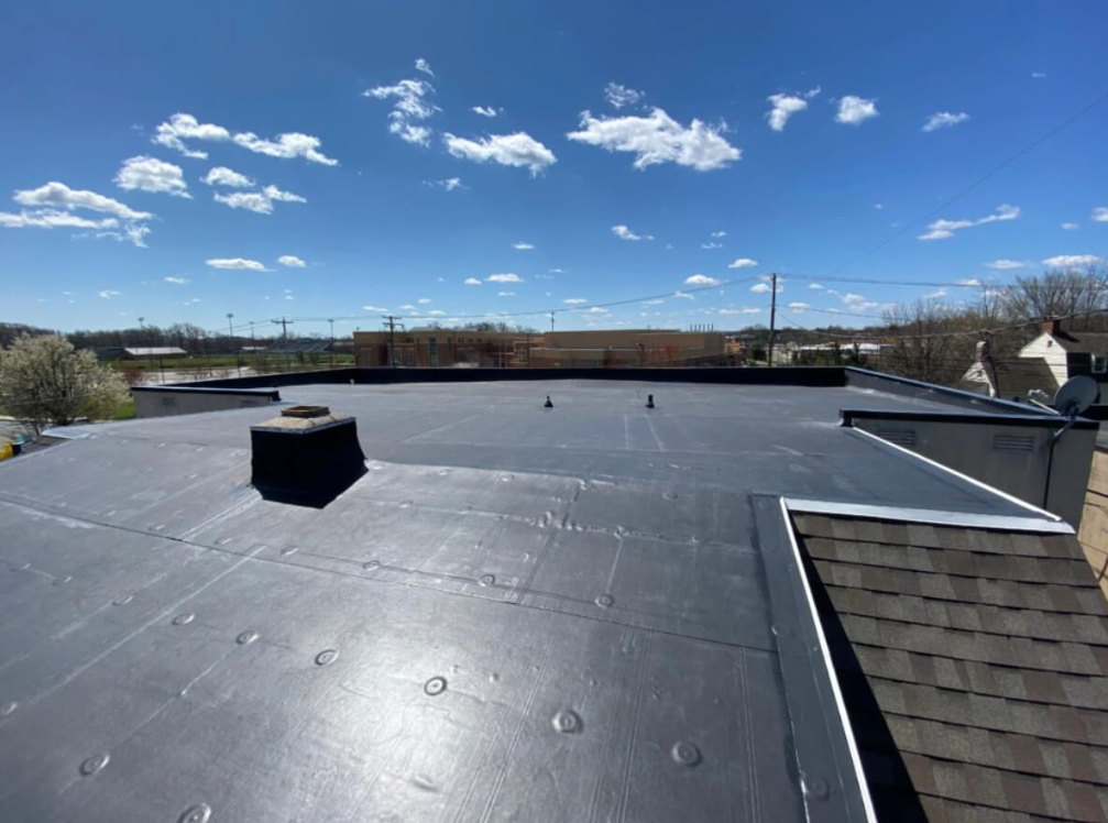 Force 5 Roofing EPDM flat roof installation — clean black membrane with mechanical fasteners, parapet wall and adjoining shingle roof visible, Colorado blue sky overhead
