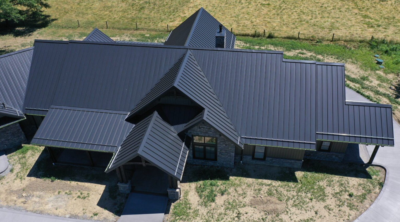 Aerial view of a Force 5 Roofing standing seam metal roof installation on a multi-gable custom home, dark matte finish across complex valleys and ridges