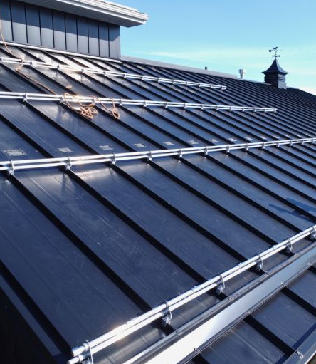 Force 5 Roofing multi-row pipe-rail snow guard system installed across a black standing seam metal roof — staggered rails distribute load and stop sliding snow in dangerous slabs