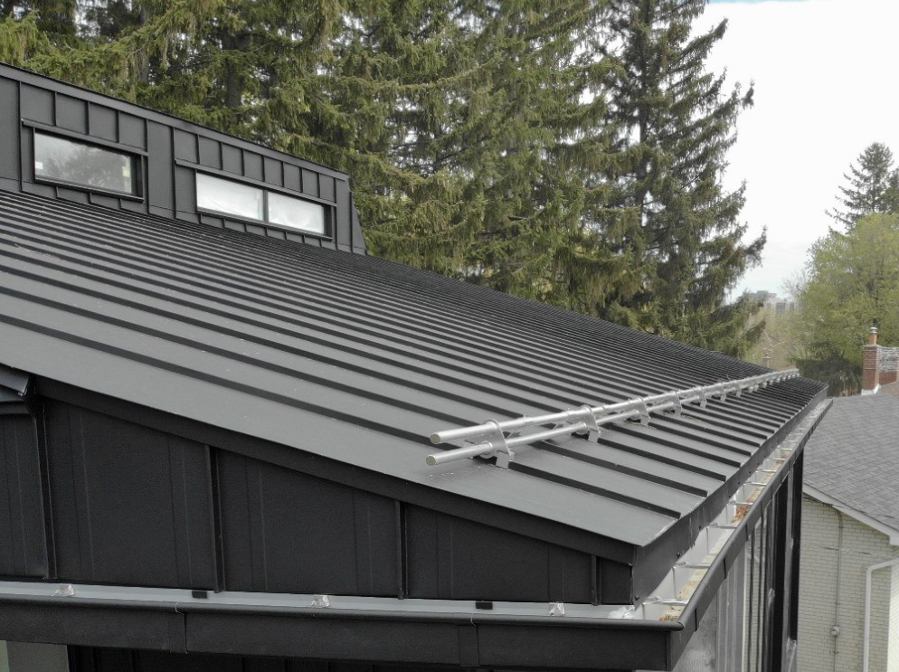 Force 5 Roofing pipe-rail snow guard system installed along the eave of a black standing seam metal roof — keeps winter snowpack from sliding off in dangerous sheets